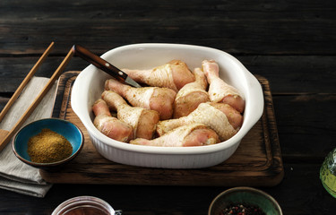 Raw chicken legs in baking dish on dark wooden table