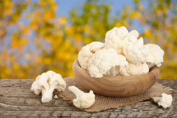 Piece of cauliflower in bowl on wooden table with blurred garden background