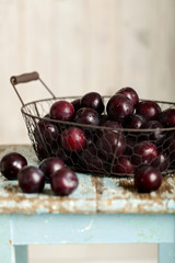 Ripe plums in a basket on a wooden background.