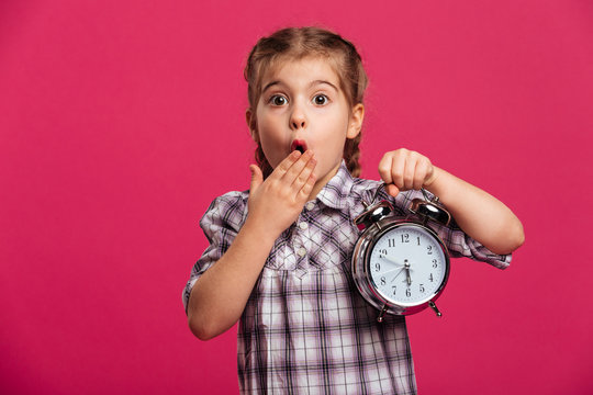 Shocked little girl child holding clock alarm.