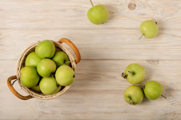 Green apples in a wicker basket on a wooden light background.