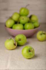 Green apples in a lilac plate on a wooden light background.