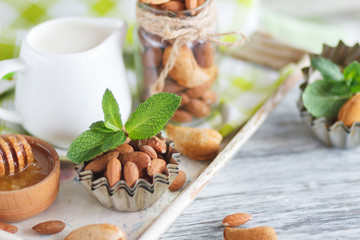 Honey in the wooden bowl, mint leaves, almonds and jar with milk on the wooden tray
