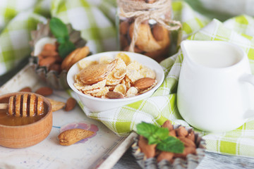 Honey in the bowl, muesli, mint leaves, almonds and jar with milk on the wooden tray