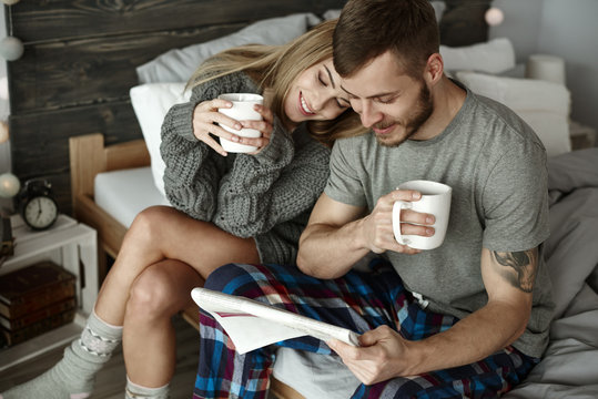 Affectionate couple with coffee reading newspaper