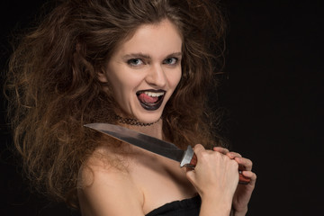 Obraz premium Beautiful girl with makeup as a witch smiles and holds a knife on a black background for the holiday of Halloween