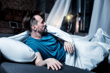 Breaking into house. Serious alarmed bearded man lying in bed and looking at the window and the...