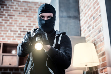 Stealing. Angry dark-eyed professional masked burglar wearing black gloves and holding a torch...