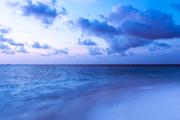 Obraz premium Tropical island at dawn. Beautiful bright sunrise over a tropical beach. Ocean and white sand. Clouds of gentle color over the sea.