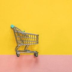 Self-service supermarket full shopping trolley cart on pink and yellow background. flat lay.