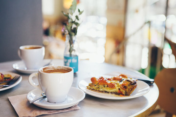 Close-up of a breakfast for two persons in a nice cafe, warm quiche and coffee, no people blurry background. Film effect.