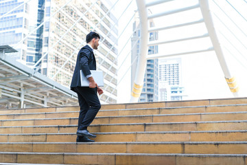 Business man celebrating success. Young businessman walking at stairs and hold laptop computer while standing outdoors with office building in the background.