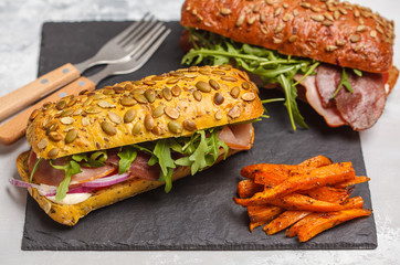 Sandwiches with ciabatta, meat, bacon, vegetables and cream sauce and sweet potato fries  on black slate. Fast food concept.