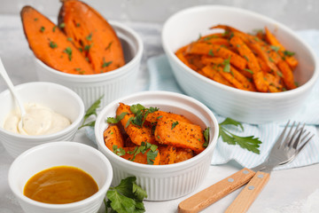 Different types of baked sweet potato with curry and a creamy garlic sauce. White dishes, light background. Healthy vegan food concept.