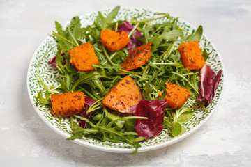 Salad of baked sweet potato with arugula. White plate, light background, top view. Healthy vegan food concept.