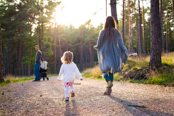 Happy young family taking a walk in a park, back view. Family walking together along forrest path...