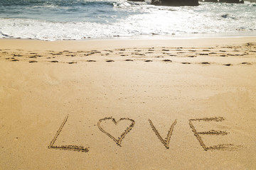 word love written on the seashore in the sand of a beautiful beach

