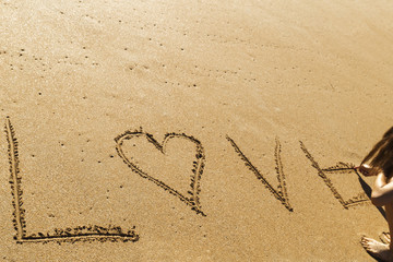 young woman writing the word love on the seashore in the sand of a beautiful beach

