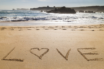 word love written on the seashore in the sand of a beautiful beach
