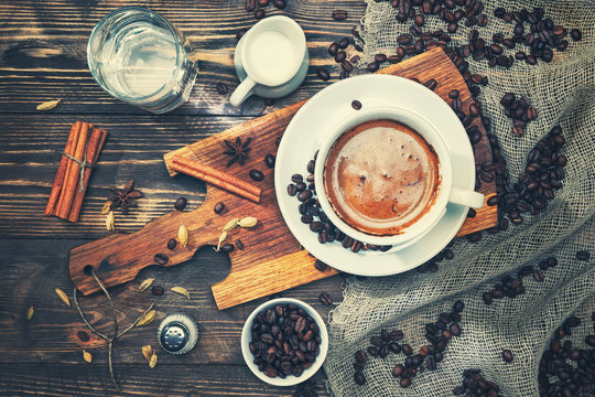 A cup of coffee on a rustic wooden table with spices, cinnamon, milk, water, salt, coffee beans. Toned.