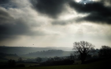 Fototapeta na wymiar Sun breaking through the mist, with a helicopter hovering in the valley. Sydling St Nicholas, Dorset, UK.