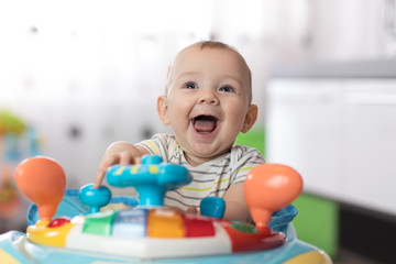 Fototapeta na wymiar Portrait of baby in baby walker. Expressive child plays toys.