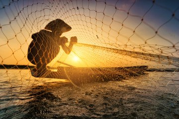 Fishermen on fishing boats use fishing equipment at sunset. - obrazy, fototapety, plakaty