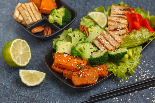 Vegetarian asian salad with sweet potato, grilled tofu, broccoli and pecan. Healthy vegan food concept. Dark background, copy space.