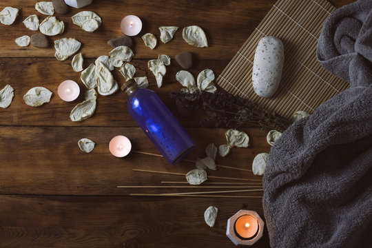 Image of a gray towel, dried rose petals, candles, soap, skin lotion, spa treatments on a wooden background