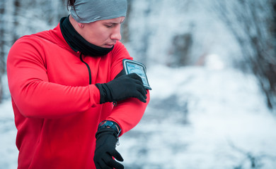 Runner using phone armband wearing warm running clothes, winter exercise outdoor