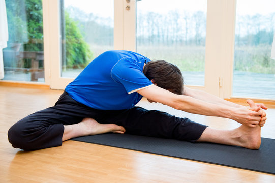 Man practicing yoga indoors in a retreat space doing Head-to-Knee Forward Bend Pose - Janu Sirsasana