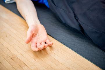Man practicing yoga indoors in a retreat space doing Corpse Pose - Savasana - closeup of a hand