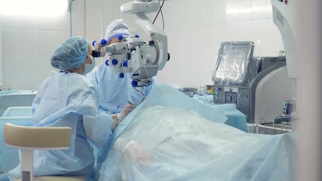 A surgeon and his assistant observe their actions through a microscope. 