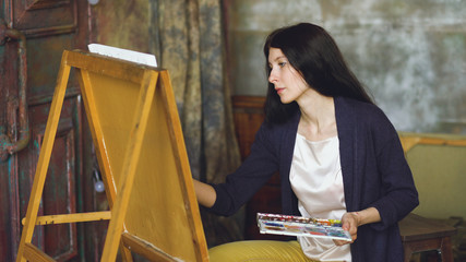 Obraz premium Young woman artist draw pictrure with watercolor paints and brush on easel canvas
