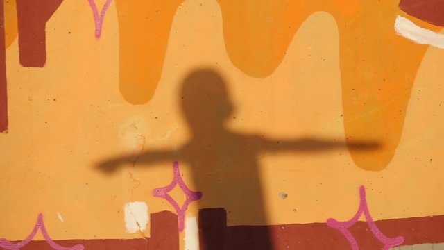 moving silhouette of a little boy with raised hands on the wall with colorful graffiti at sunset