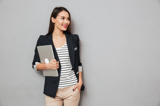 Happy business woman with arm in pocket holding laptop computer