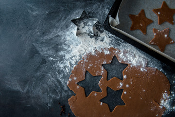 Christmas gingerbread star cookie cutter on flour, gingerbread dough with star shaped cutout and cookie star cut out of the dough in sheet pan. Dark background, top view, flat lay.