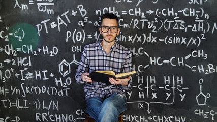 Young scientist man read book in chemical and mathematical equations wall room interior