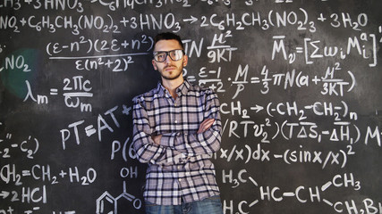 Young scientist man posing in chemical and mathematical equations wall room interior