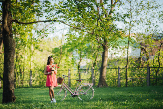 Cath the moment. Young woman in a pink dress with a bike with flowers in a summer park. Family vacations. Europe tradition.