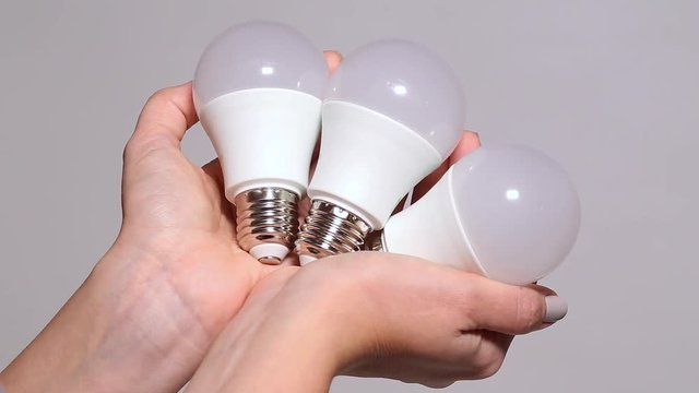Closeup view of female hahds holding three new white energy saving LED lamp of 10W isolated on white background.