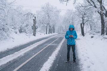 teenager with smartphone and blue jacket, snow day on the road