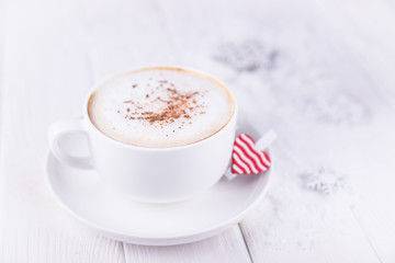 Happy Valentine's day. White cup with cappuccino and red heart on a white wooden background. Free space