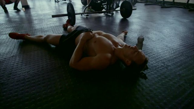 Muscular man tired after intense workout in cross fit gym. Bodybuilder taking break after cross training. Lying on gym floor after exercising sessi