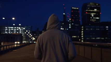 Camera follows a hooded male jogging early in the morning in the city, in slow motion