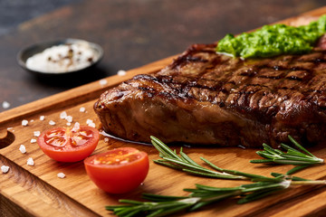 Grilled Black Angus Steak with tomatoes, garlic with chimichurri sauce on meat cutting board.