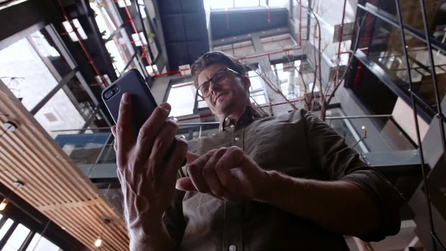 Low angle view of young man texting on his mobile phone and smiling. Creative businessman using cell phone during break.