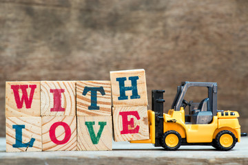 Yellow toy forklift hold letter block H and E to complete word with love on wood background