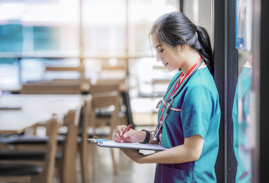 Nurse in purple uniform standing near glass window and writing on medical chart