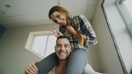 POV of happy smiling and beautiful couple take selfie portrait on smartphone camera while girl sitting on man's neck at home